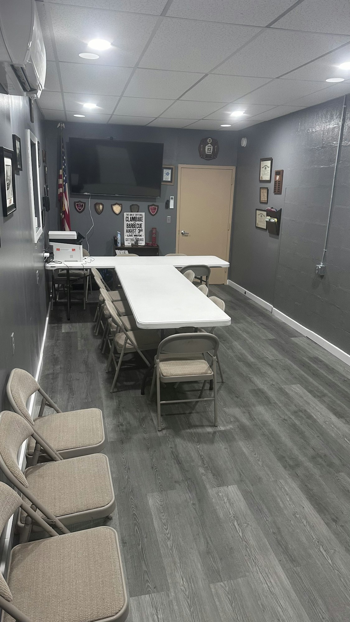 A room with folding tables, chairs, a TV, and wall decorations.