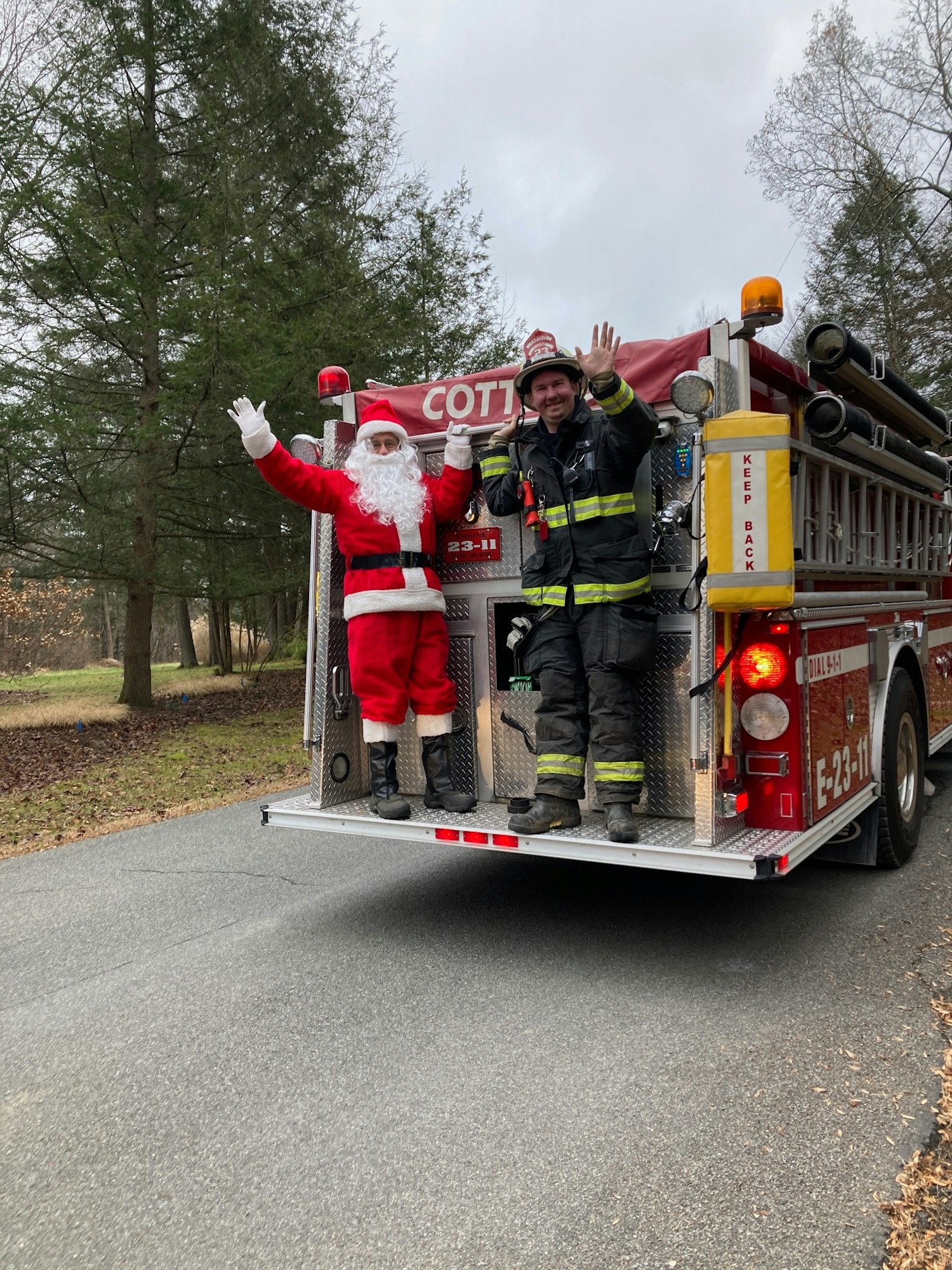 Santa Claus and a firefighter waving from the back of a fire truck.