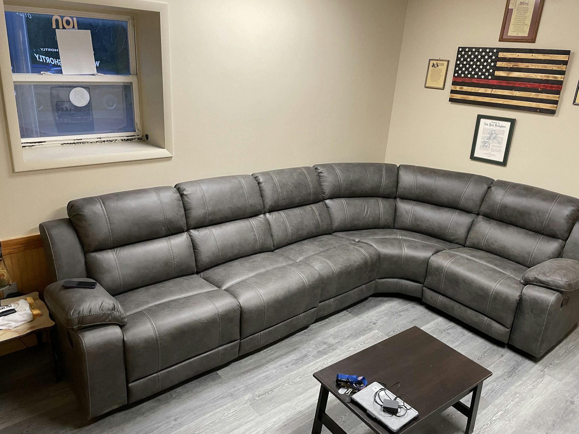 A gray sectional sofa, wooden coffee table with items on top, window, and American flag-themed wall art in a room.