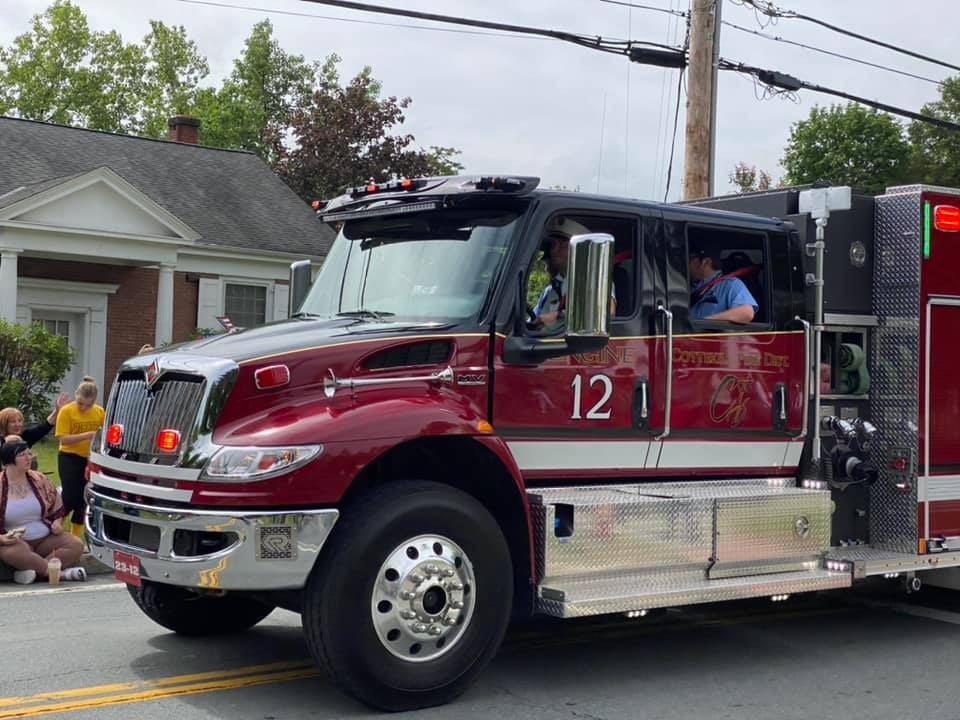 A red fire engine with number 12 on the side, people visible inside, driving past spectators.