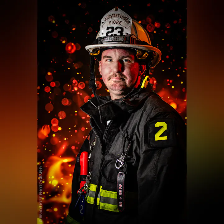 A firefighter in uniform with "Assistant Chief" on the helmet, set against a fiery background.