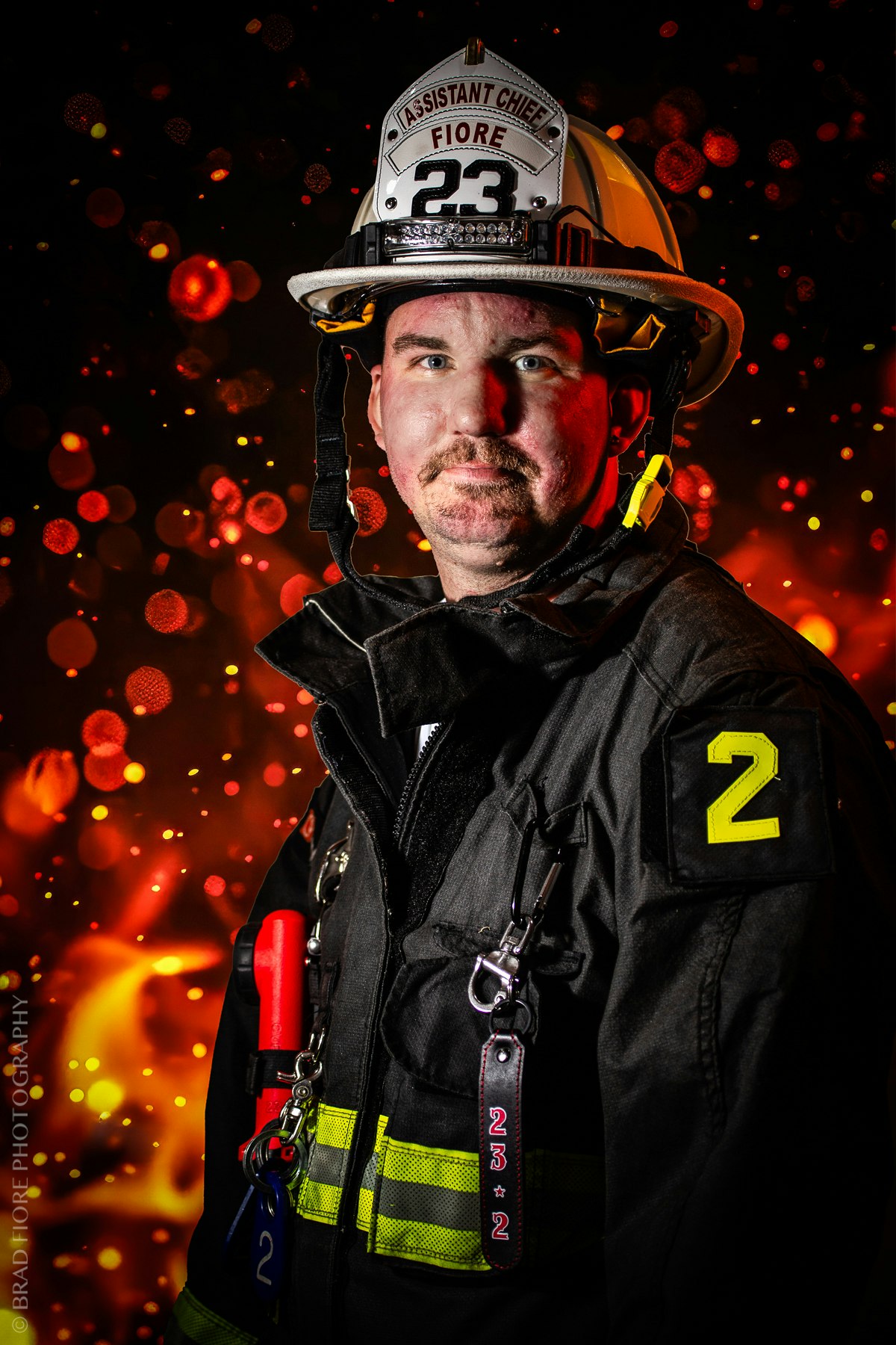A firefighter in uniform with "Assistant Chief" on the helmet, set against a fiery background.