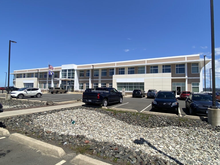 A modern two-story building with a parking lot, American flag, and clear blue sky.