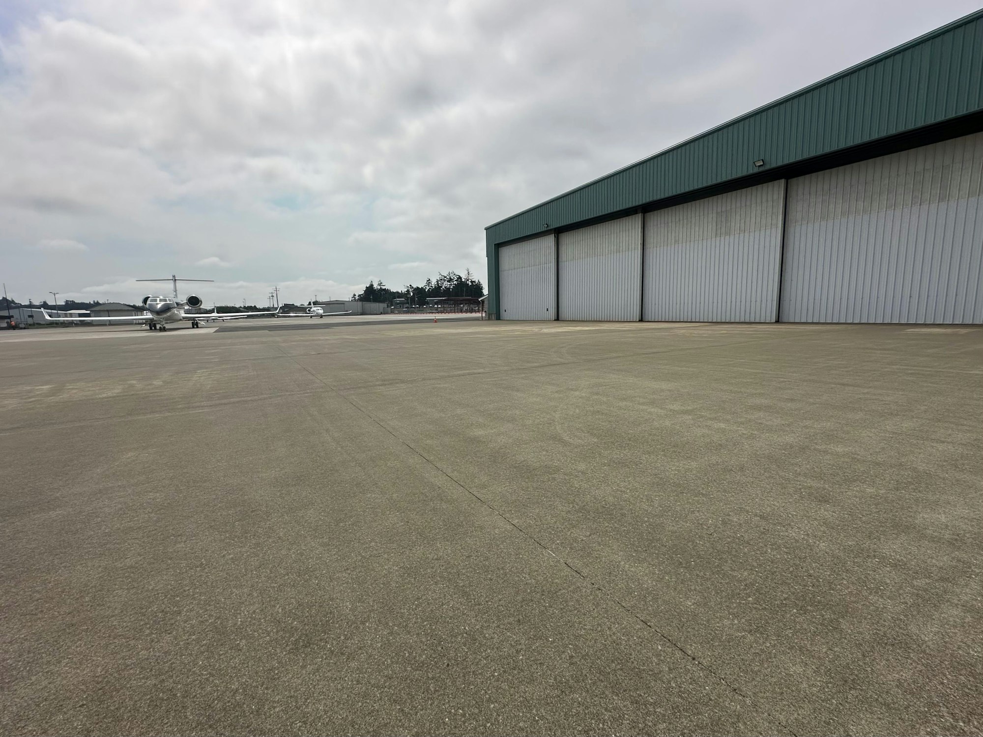 Airplane on tarmac beside a large hangar under a cloudy sky.