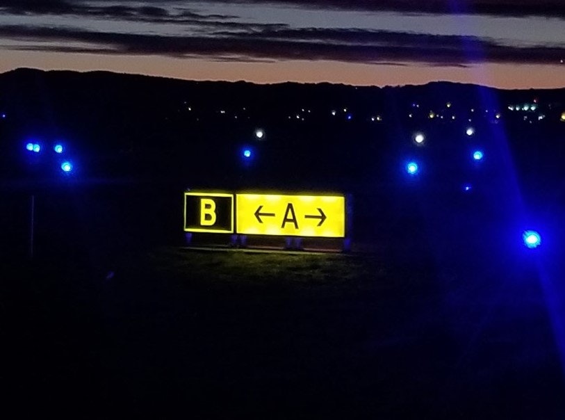 Illuminated directional signs with letters "A" and "B" against a twilight sky, surrounded by blue lights.