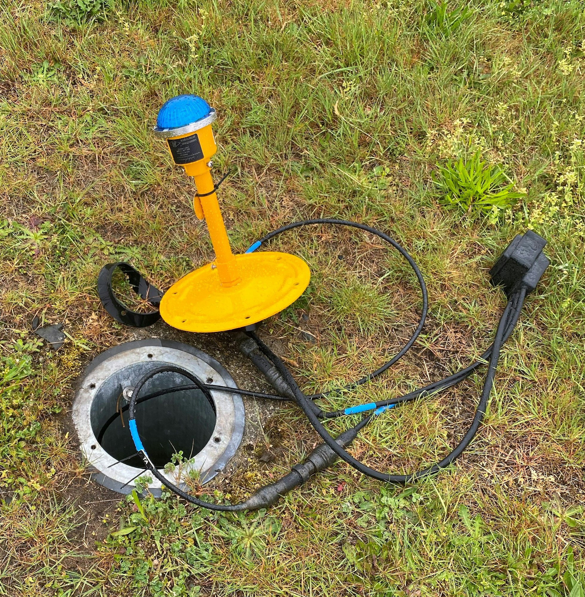 A metal detector next to an open ground hatch, surrounded by grass.