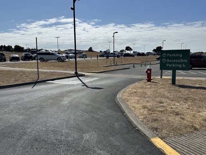 Southwest Oregon Regional Airport parking lot construction zone near the terminal entrance. Includes a sign, fire hydrant, parked cars, and cones.
