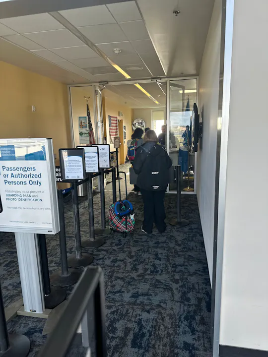An airport security checkpoint with signs for authorized persons, passengers waiting, and a visible American flag.