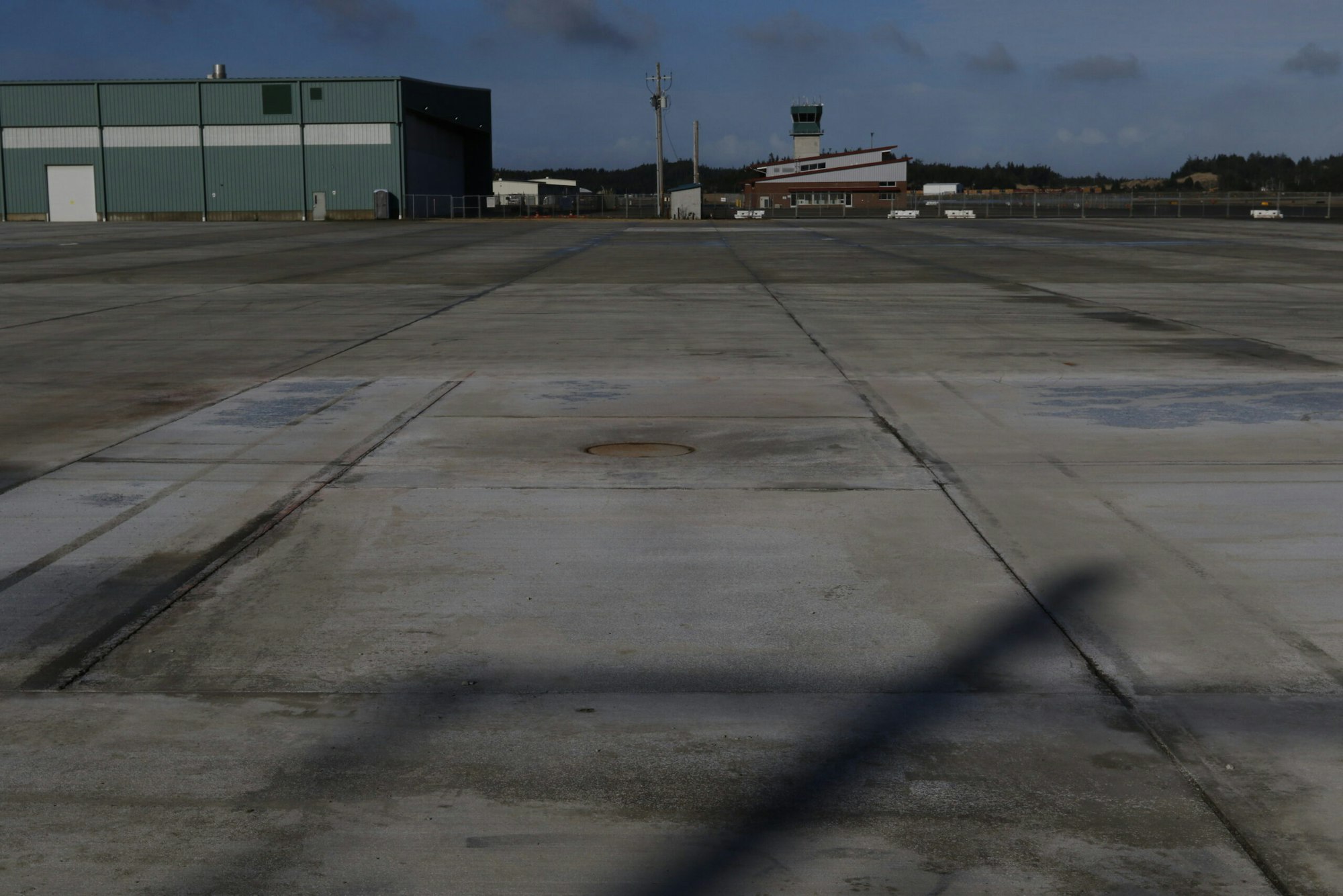 Empty airport apron, hangar, control tower, shadow of aircraft's tail.