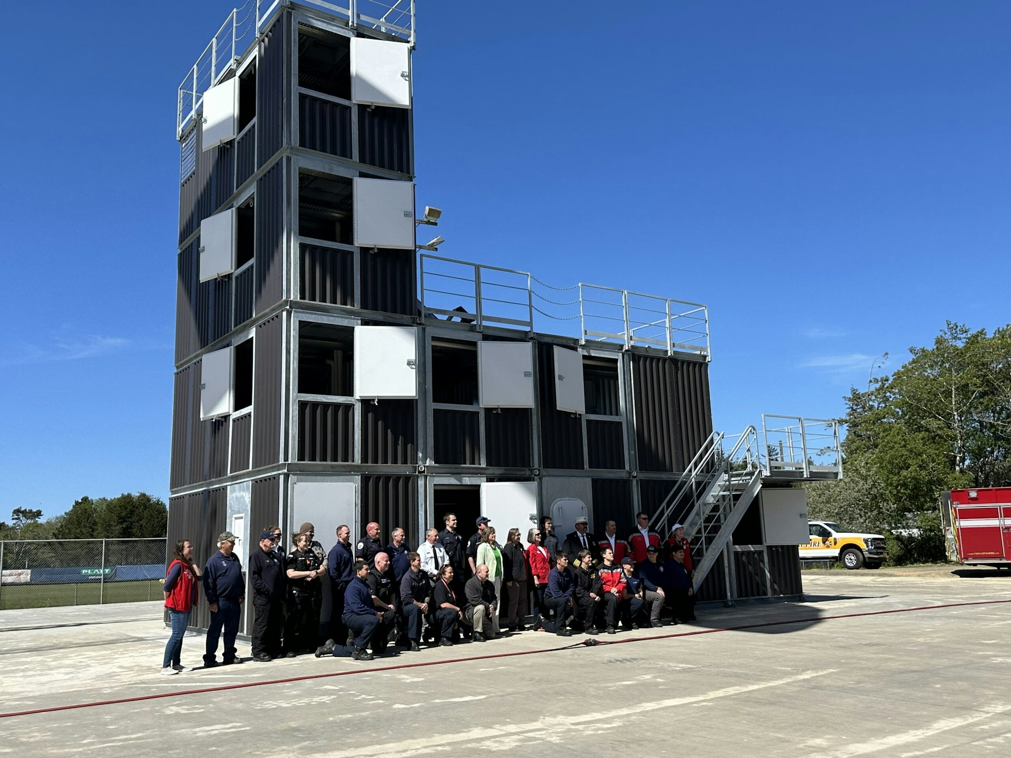 Group of people posing in front of a multi-story training structure with clear skies.