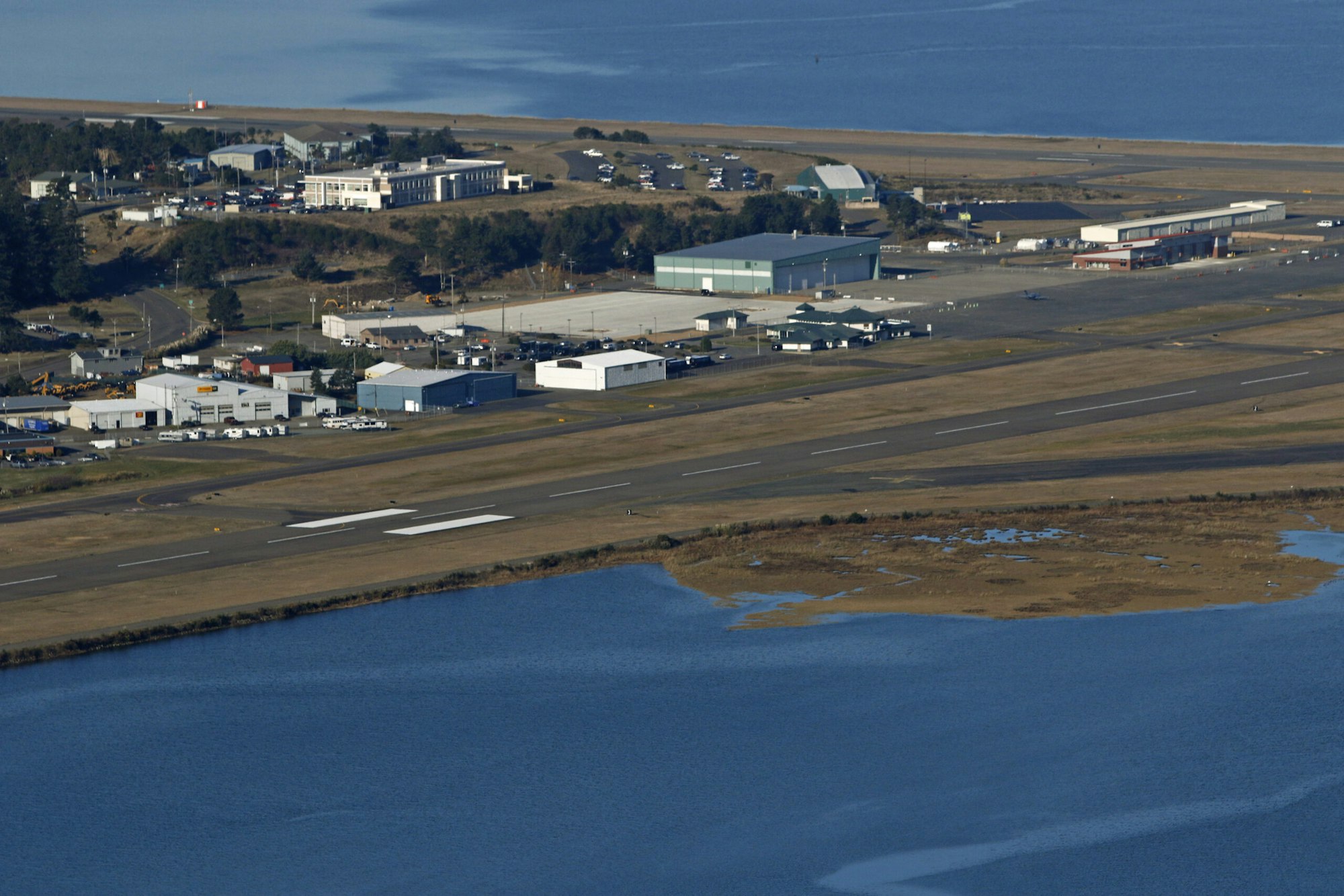 Aerial view of an airport with adjacent buildings, runways, and surrounding water.