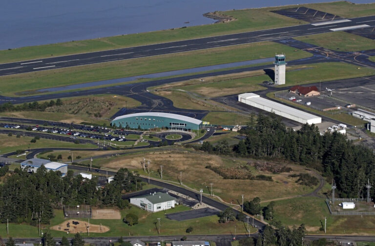 Aerial view of an airport with runways, a control tower, a terminal building, and parking lots surrounded by greenery.