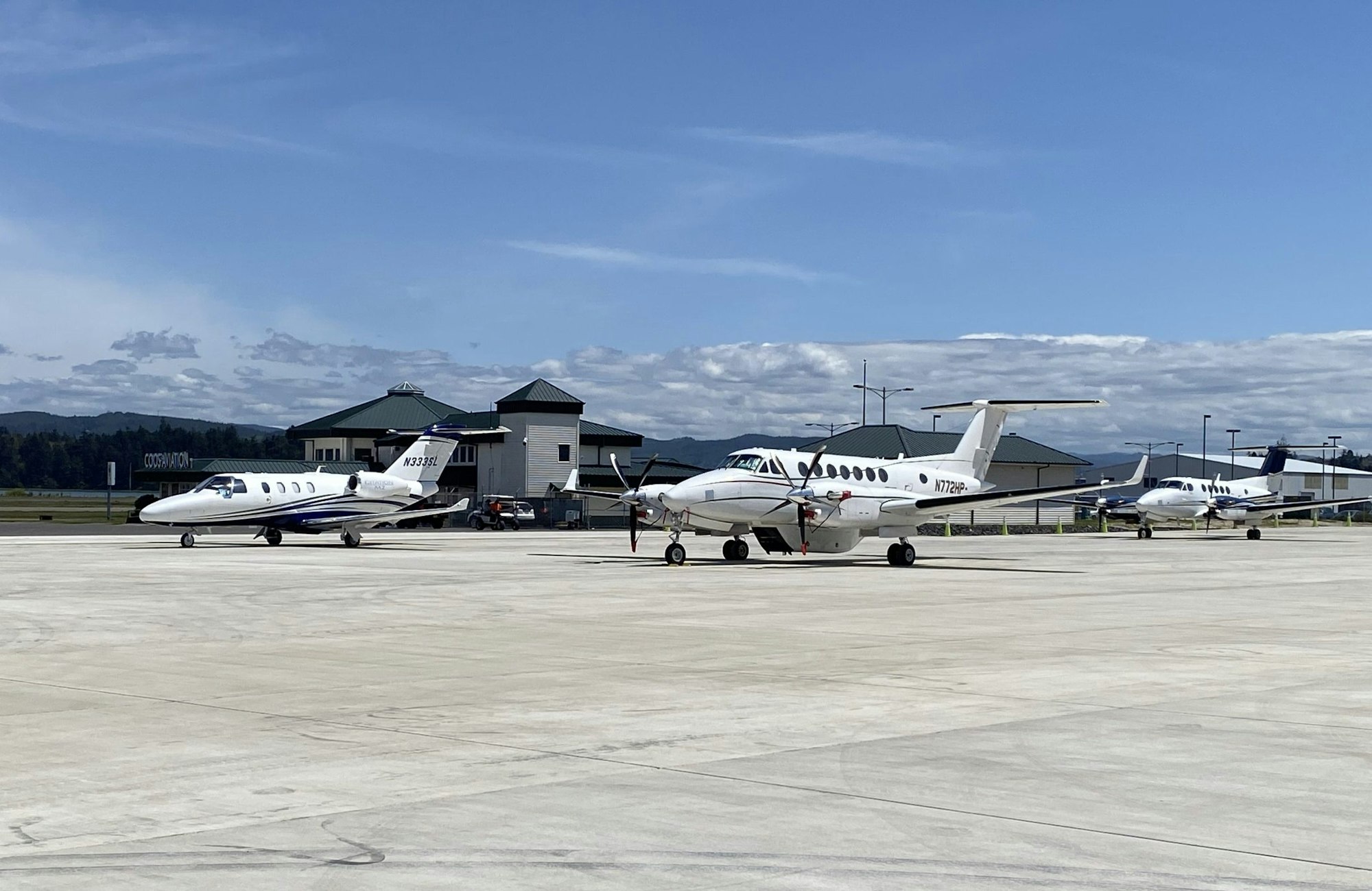 Private jets parked at an airport with clear skies and mountains in the background.
