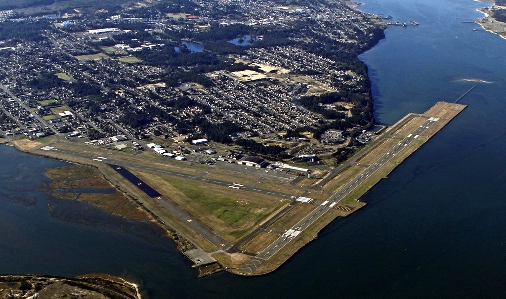 Aerial view of an airport runway beside a body of water, with adjacent urban development.