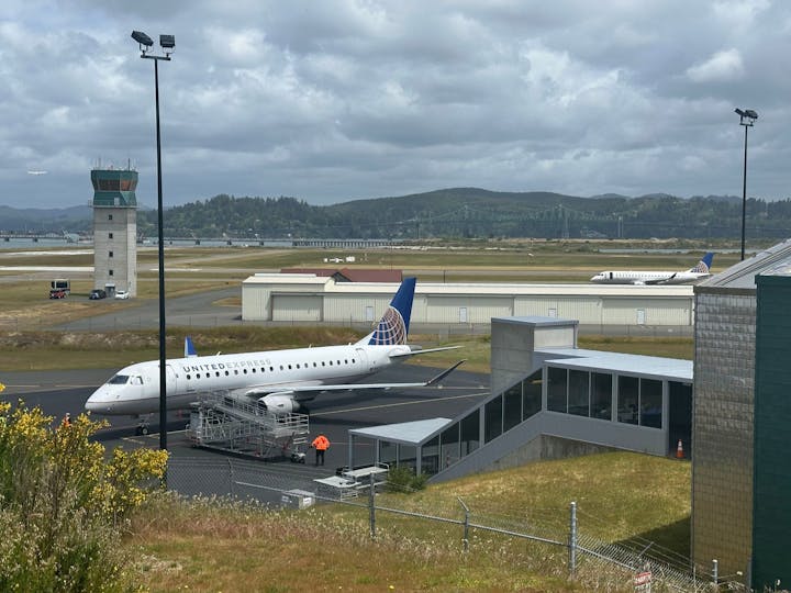 Airport scene with a United Express airplane, control tower, and a glimpse of a bridge in the background.