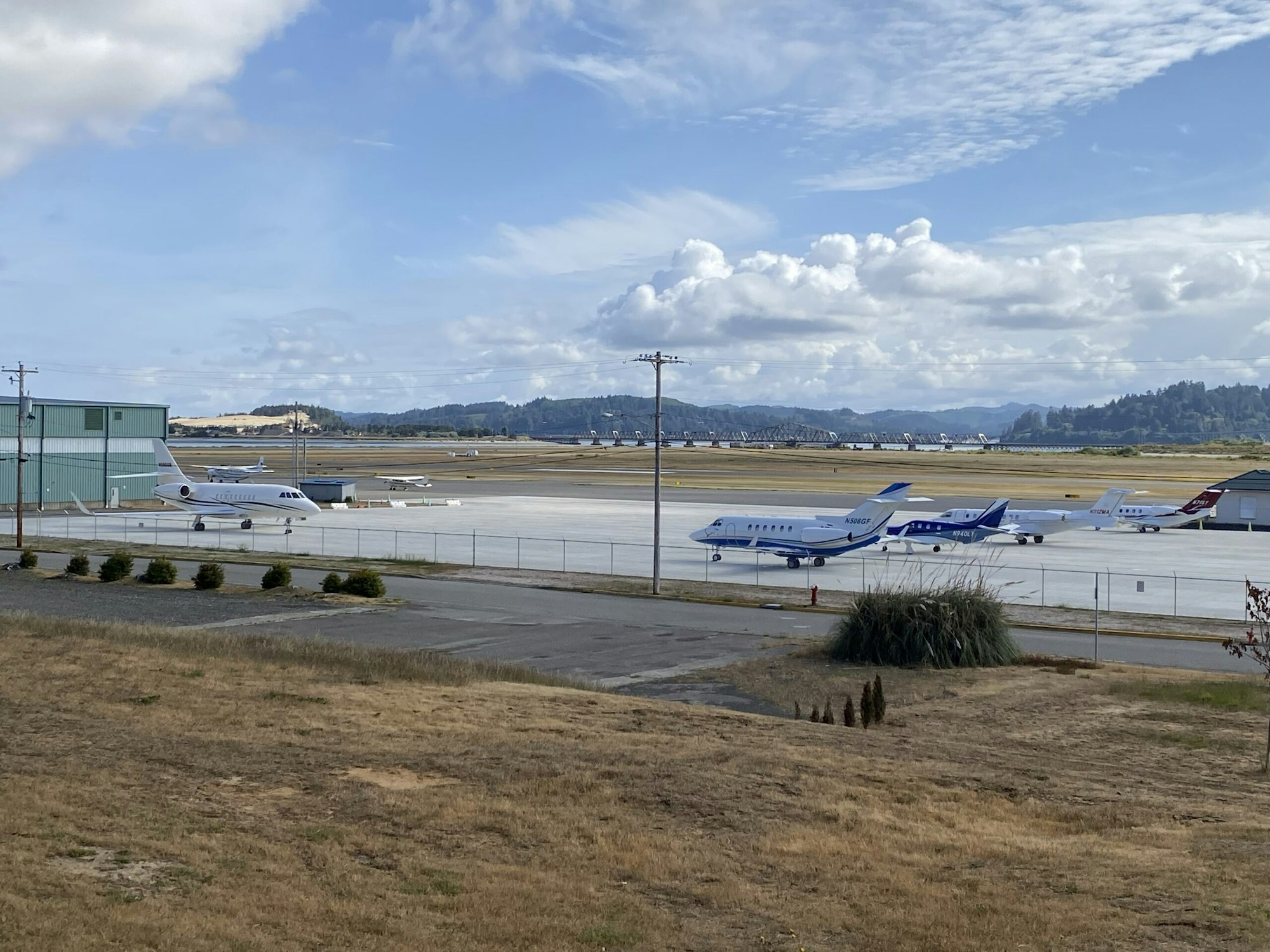Aircraft on tarmac, airport facilities, grassy area, cloudy sky.