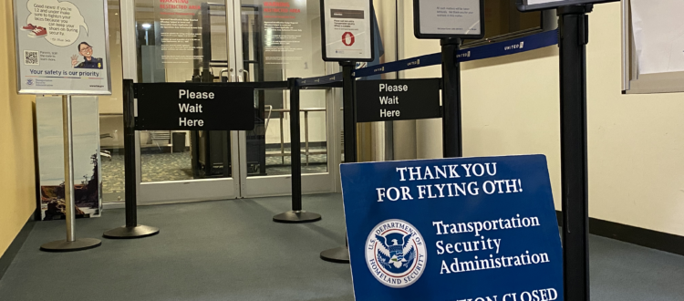 An empty airport security checkpoint area with signs, a closed notice from TSA, and stanchions.