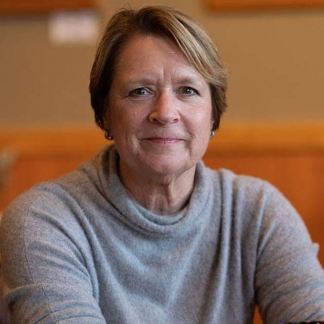 A smiling person with short hair wearing a grey turtleneck, indoors.