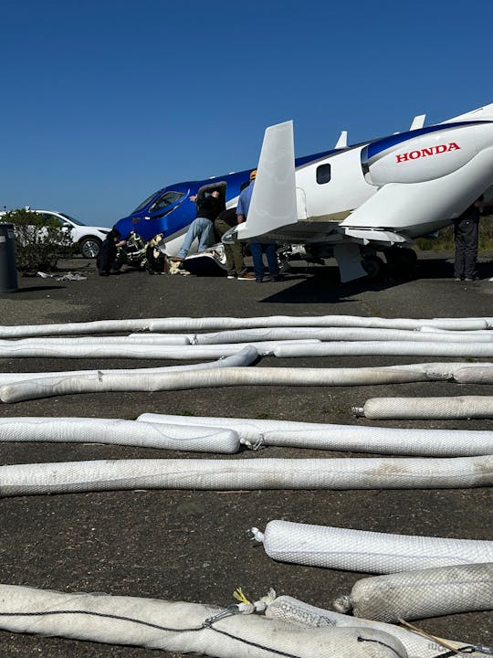 A small aircraft with people around it on the ground, surrounded by several white cylindrical objects.