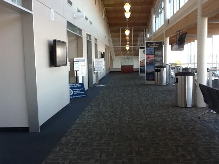 An indoor hall with posters, a carpeted floor, ceiling lights, a trash receptacle, and a bench.