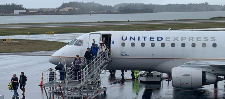 Passengers disembarking a United Express plane via stairs on a wet tarmac.