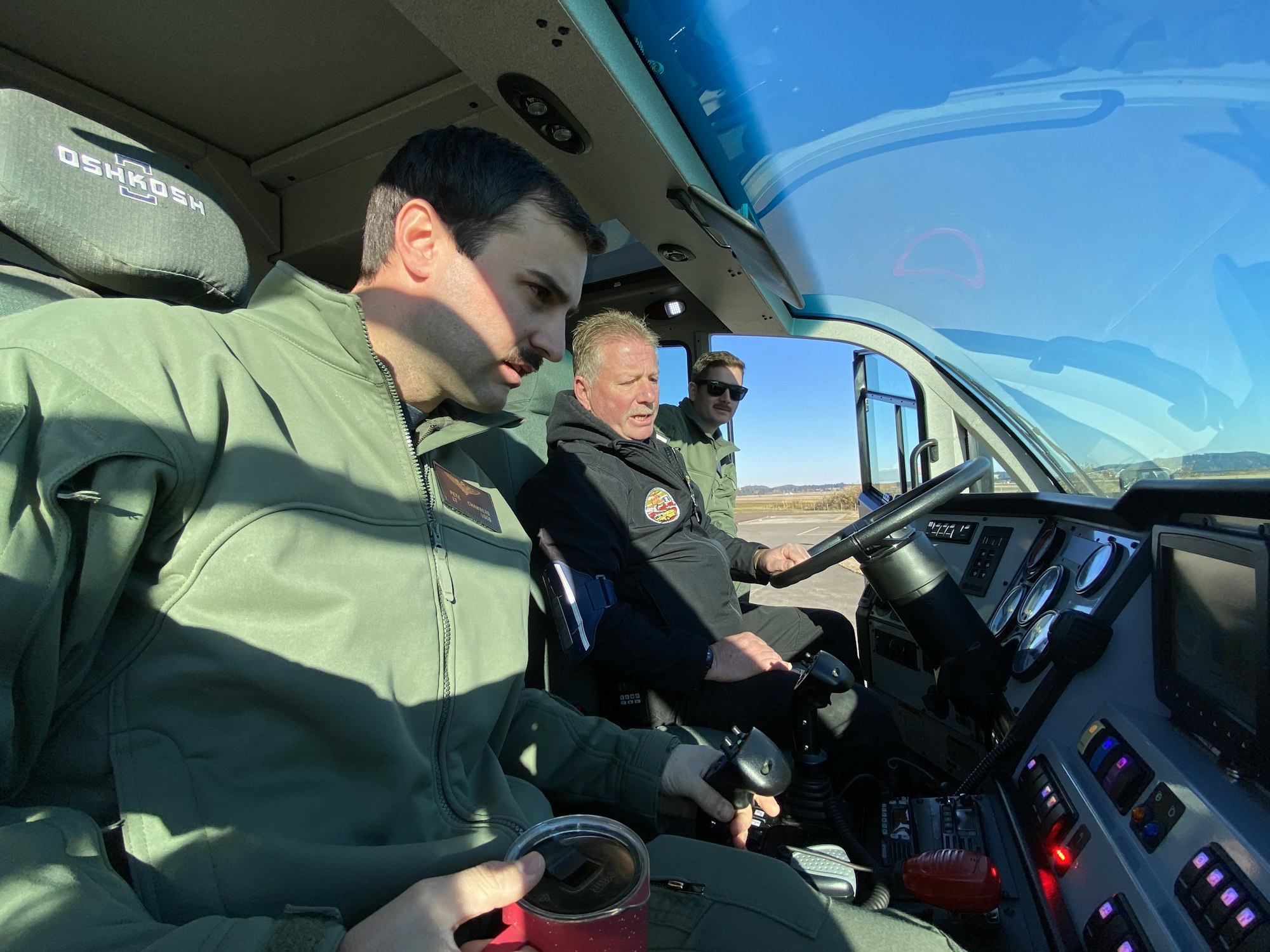Three individuals are seated inside a vehicle's cabin, examining controls, with sunlight and scenic views visible outside.