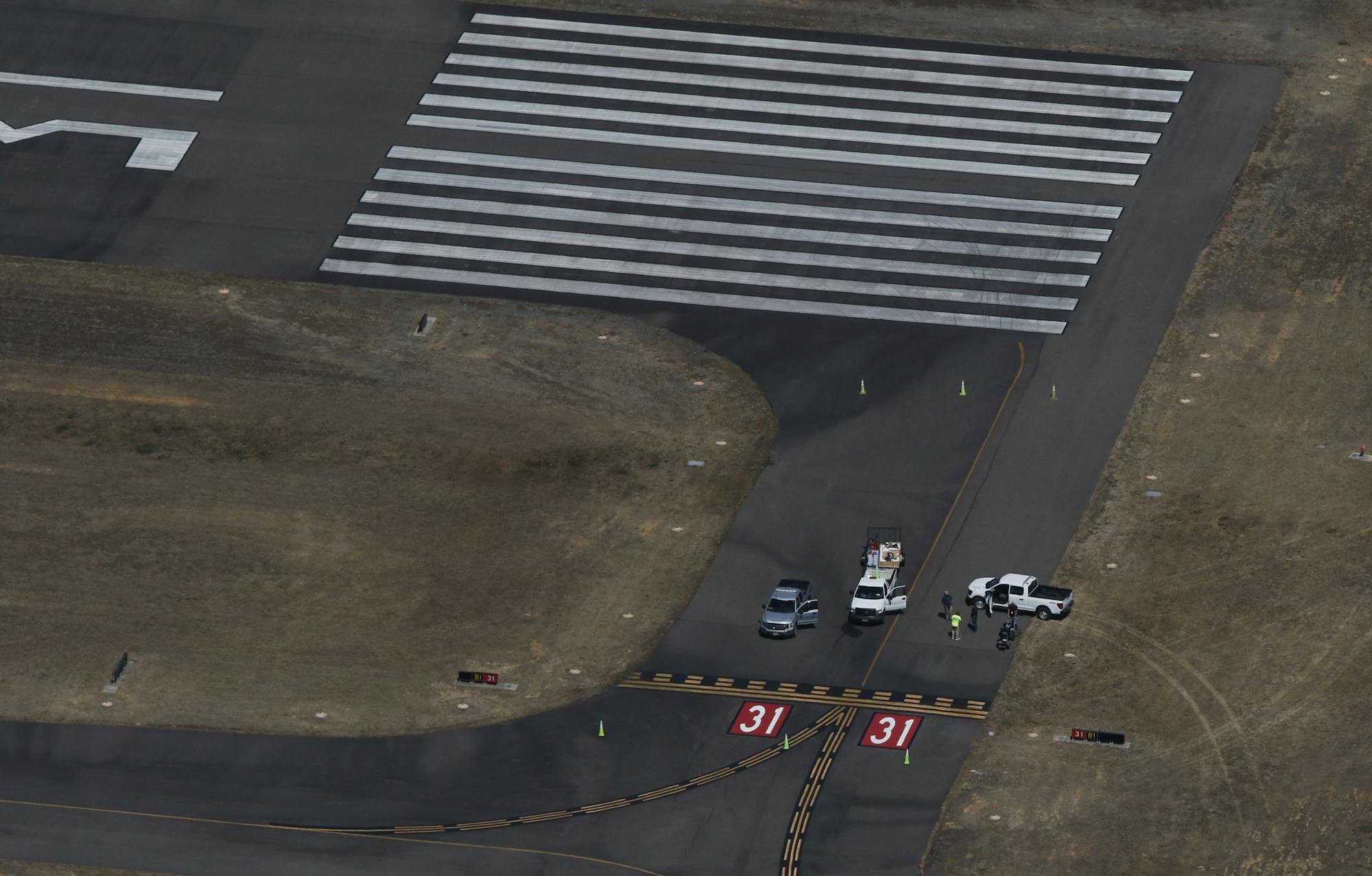 Aerial view of an airport runway intersection with vehicles and people near runway markings "31".