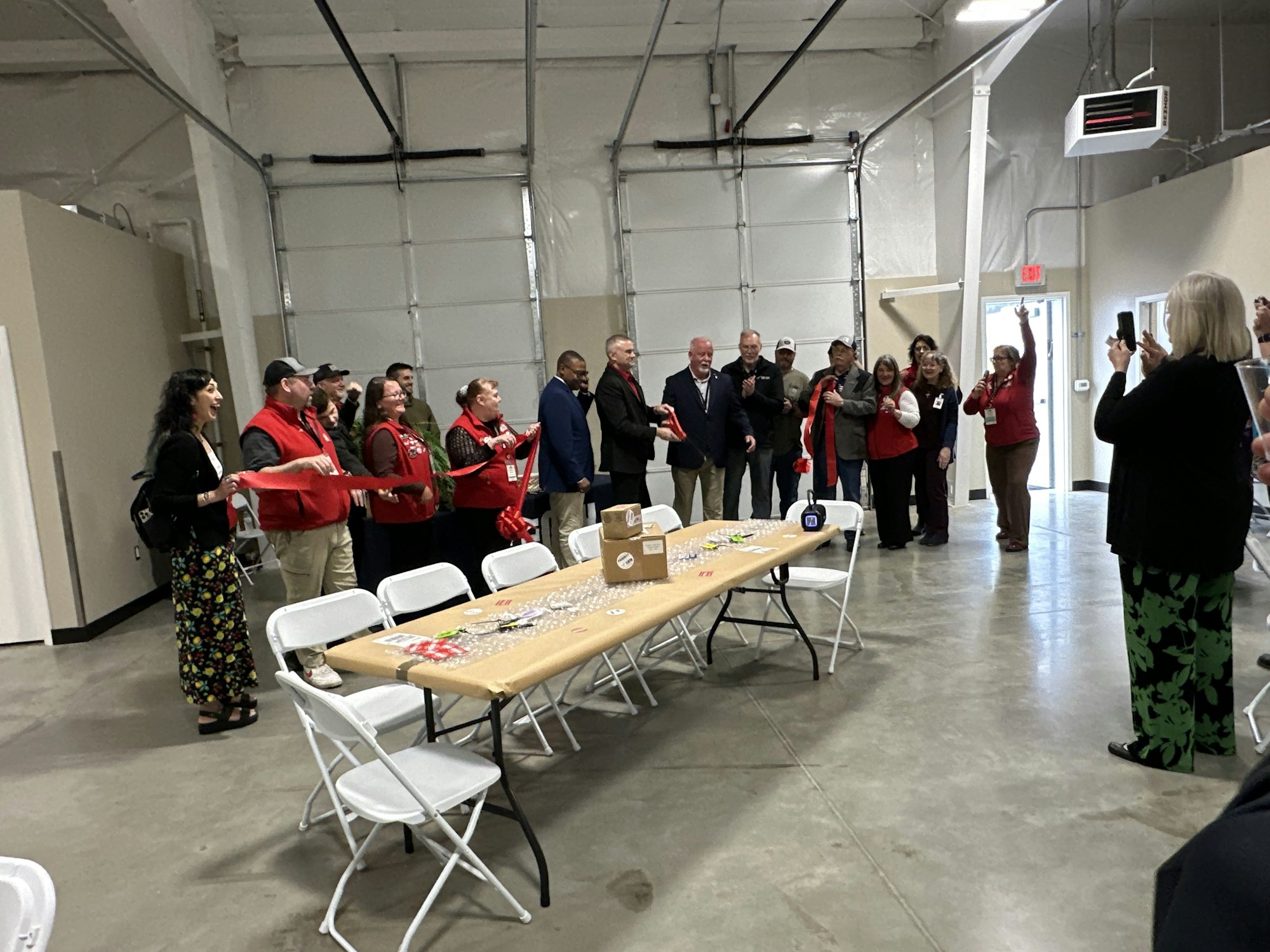 A group of people in red vests is gathered inside a large hall for a celebration, with some taking photos and cheering.