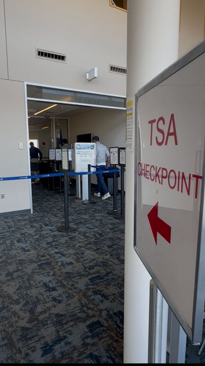 TSA checkpoint at an airport with signage and security barriers.