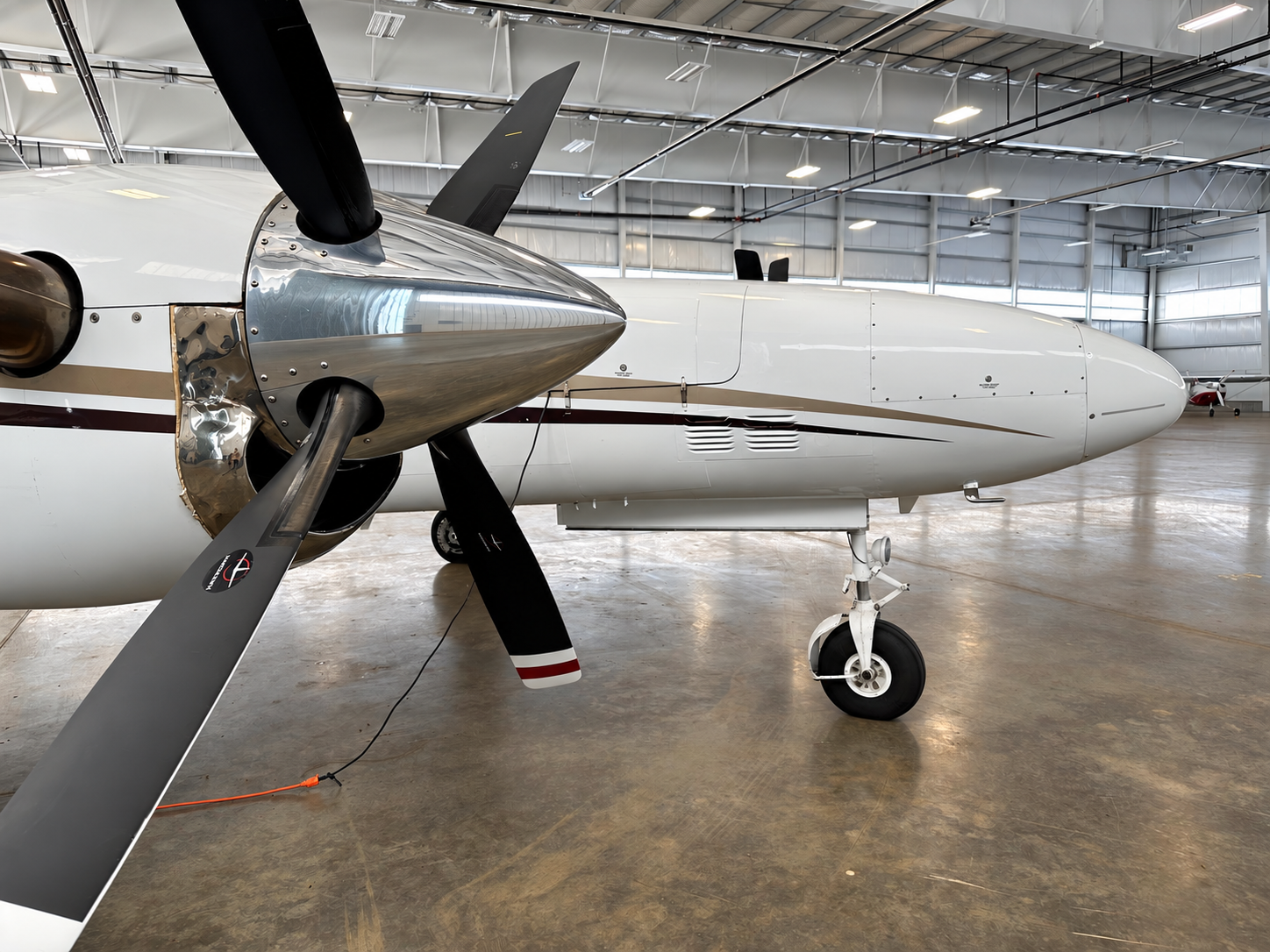 The image shows a close-up of an aircraft's propeller and engine section inside a hangar.