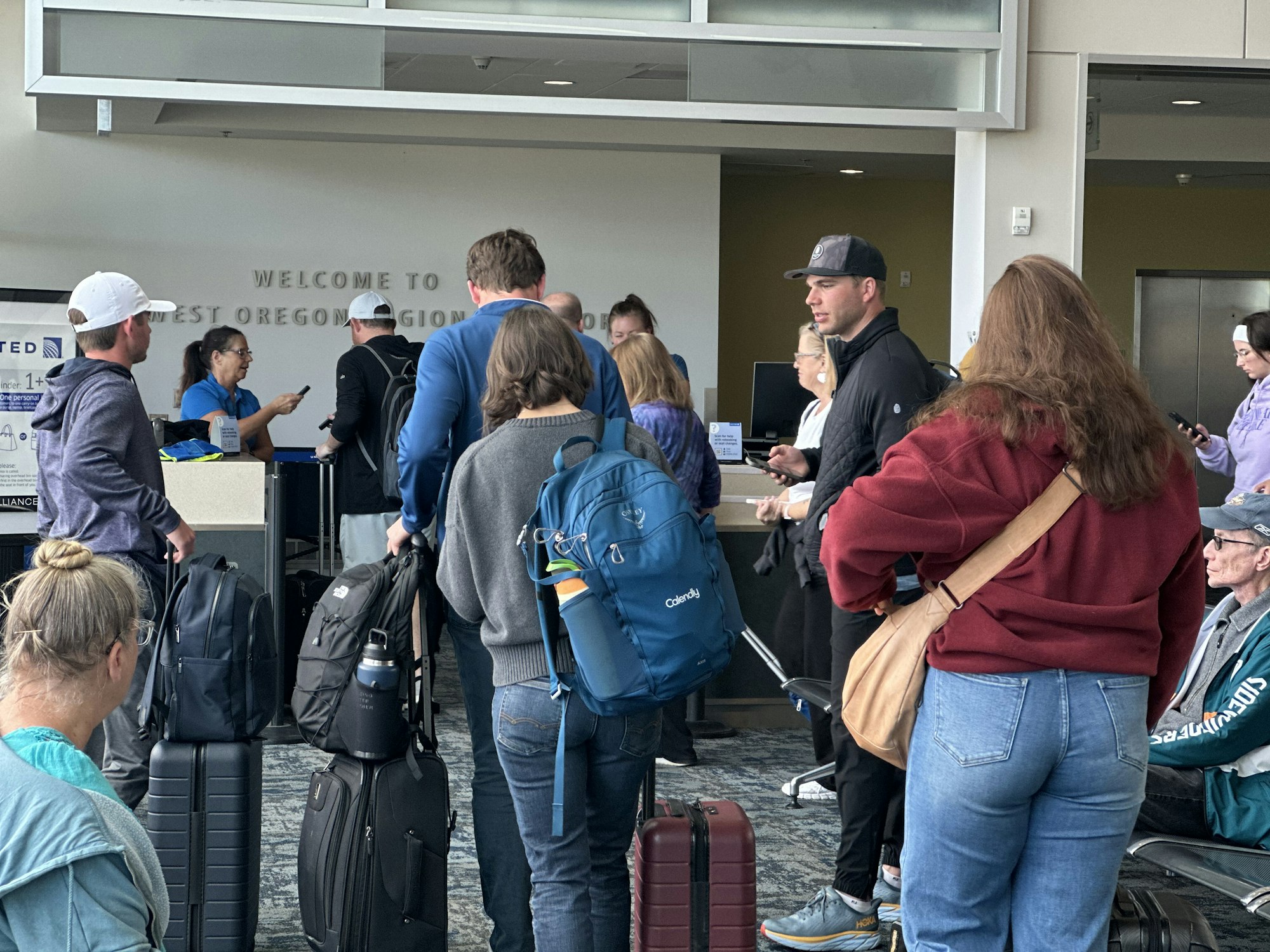 People with luggage line up at an airport gate labeled "United" at East Oregon Regional Airport.