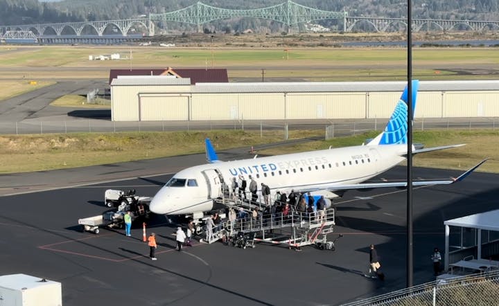 United Express plane at an airport, passengers boarding via stairs, bridge in the background.