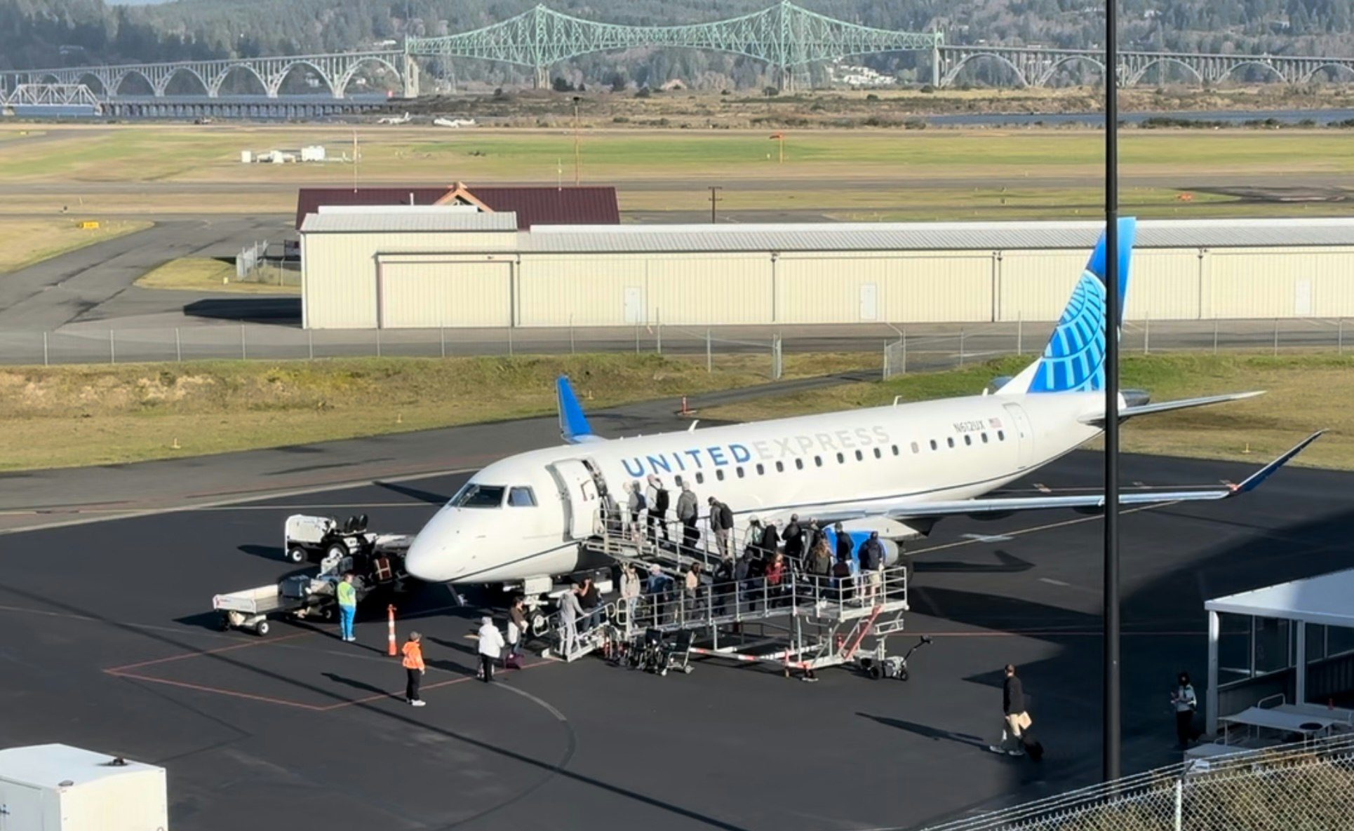 United Express plane at an airport, passengers boarding via stairs, bridge in the background.