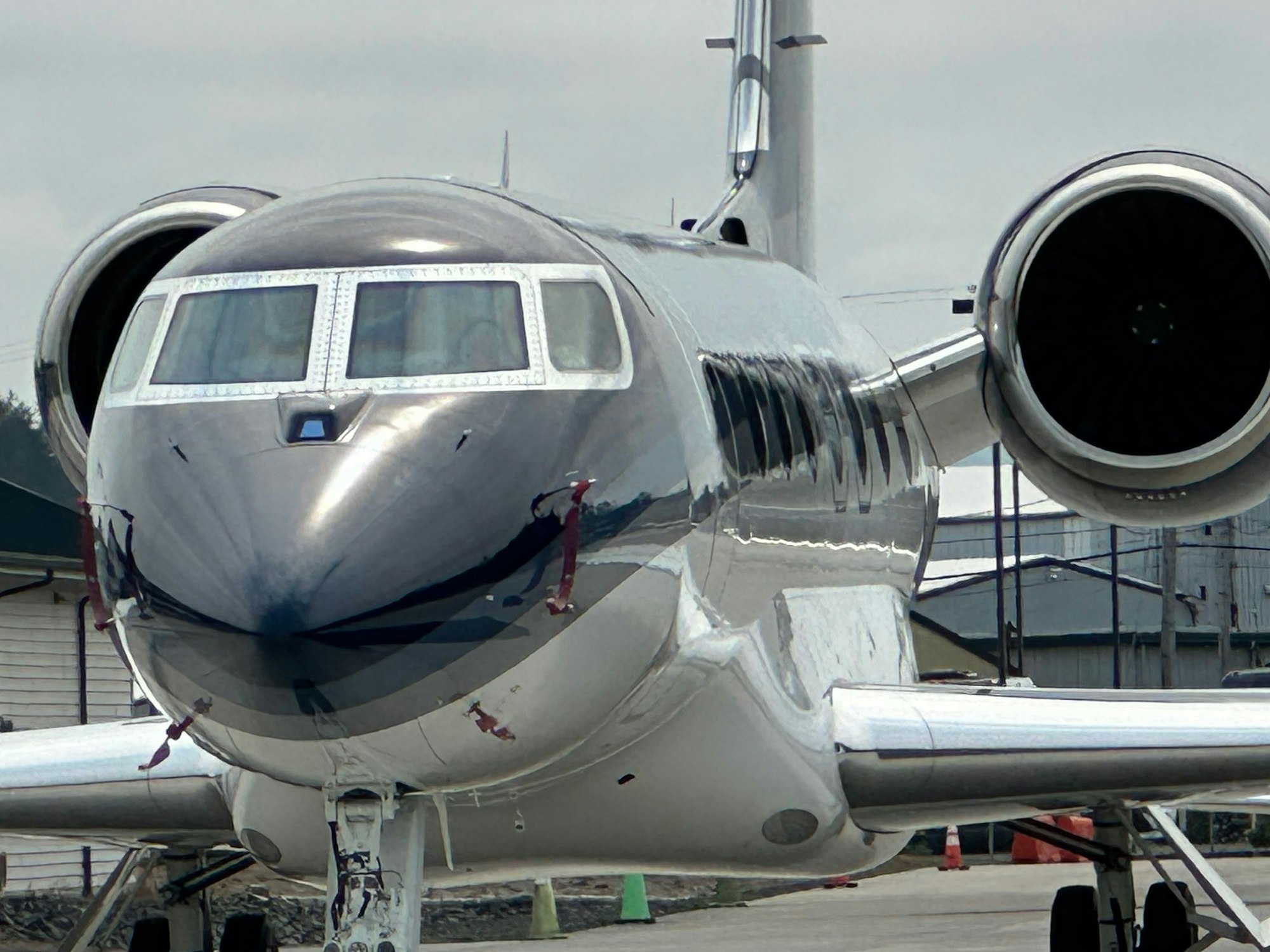 A close-up of a shiny, silver private jet parked on the tarmac with large jet engines visible.
