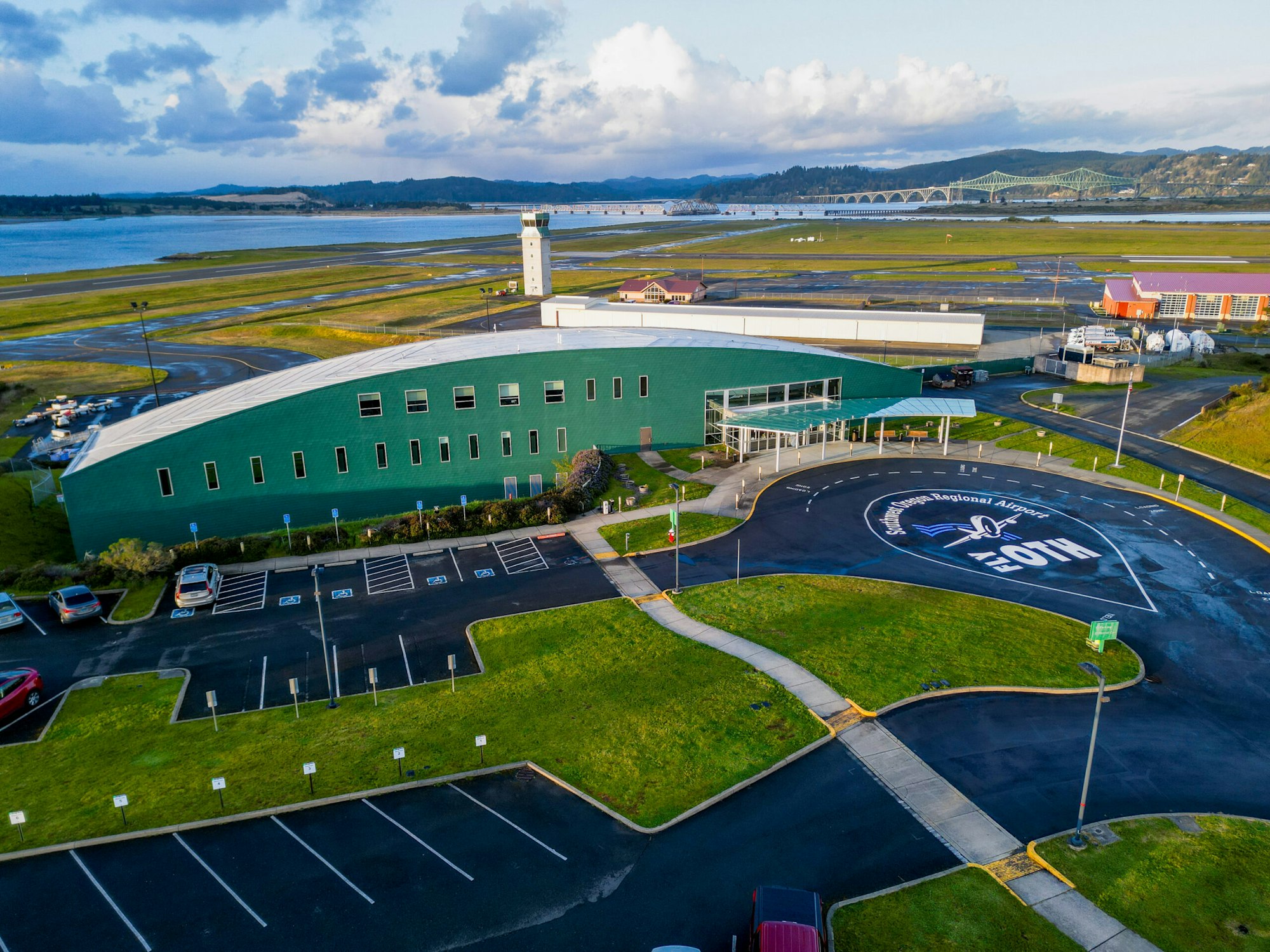 An aerial view of an airport with a control tower, parking lot, and logo on the pavement.