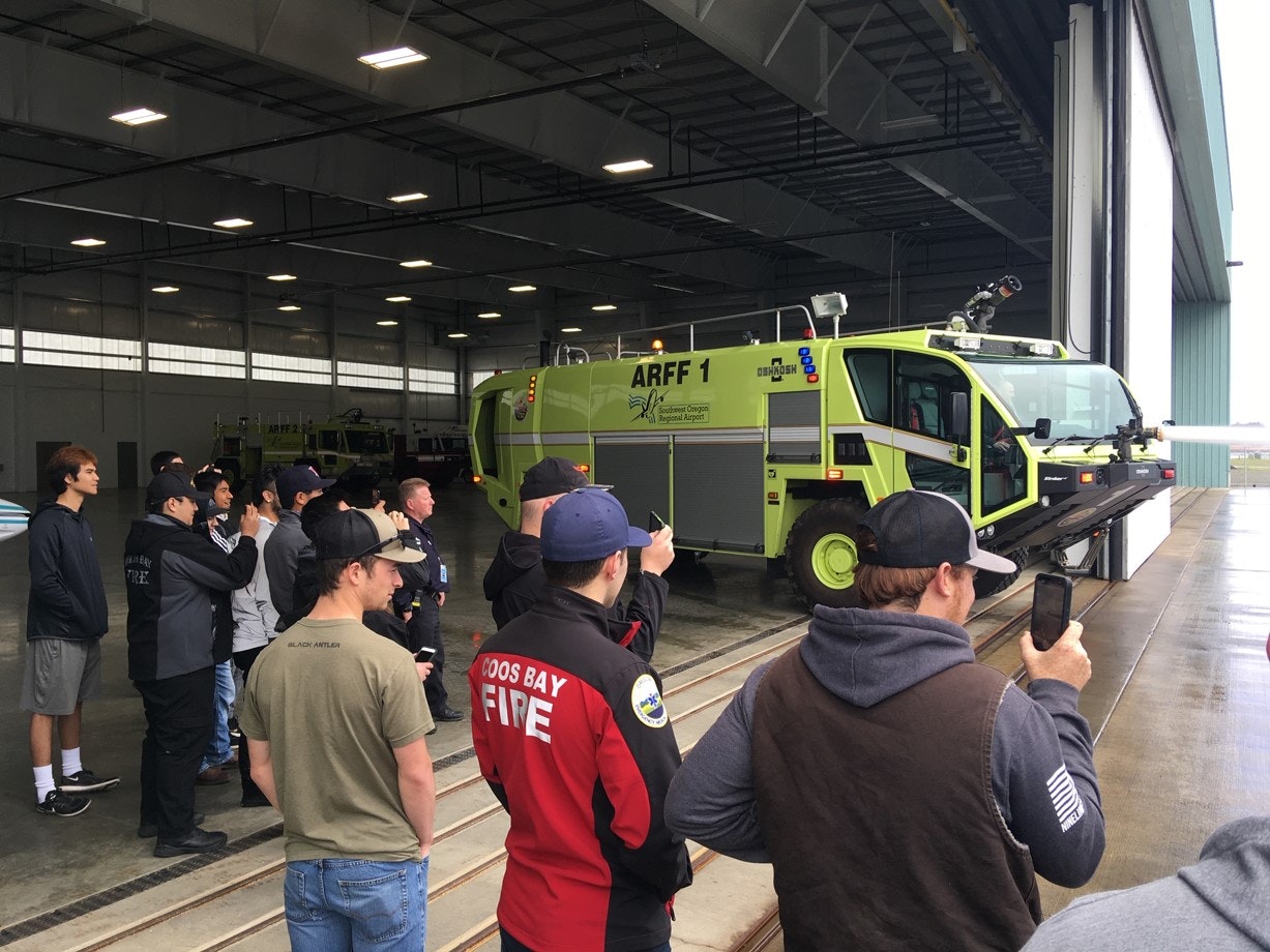 A group of people observing an airport fire rescue vehicle inside a hangar.