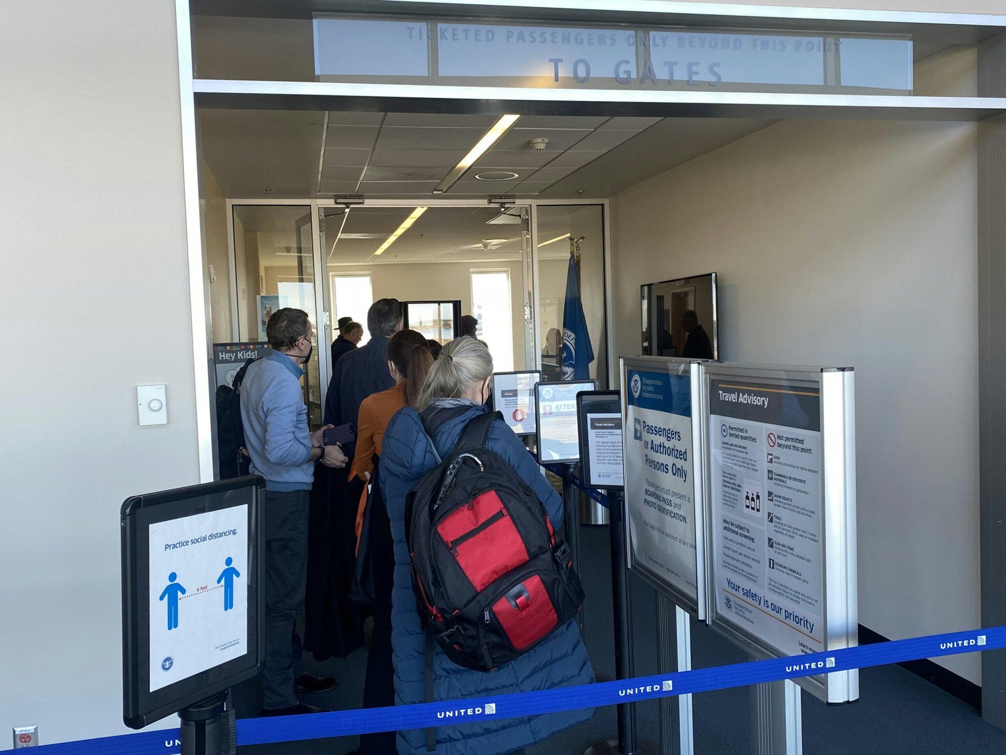 Airport boarding gate with passengers in line, signs promoting safety and social distancing.