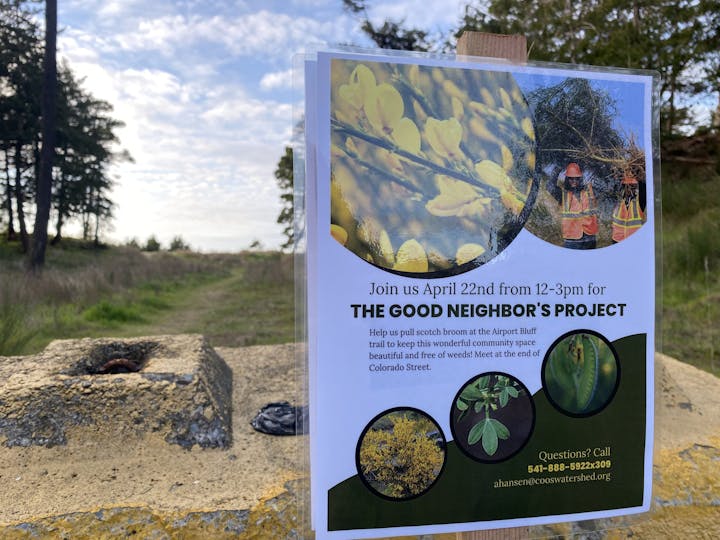 A flyer attached to a clear surface outdoors inviting people to a community event for weeding on April 22nd. Background shows a natural trail.