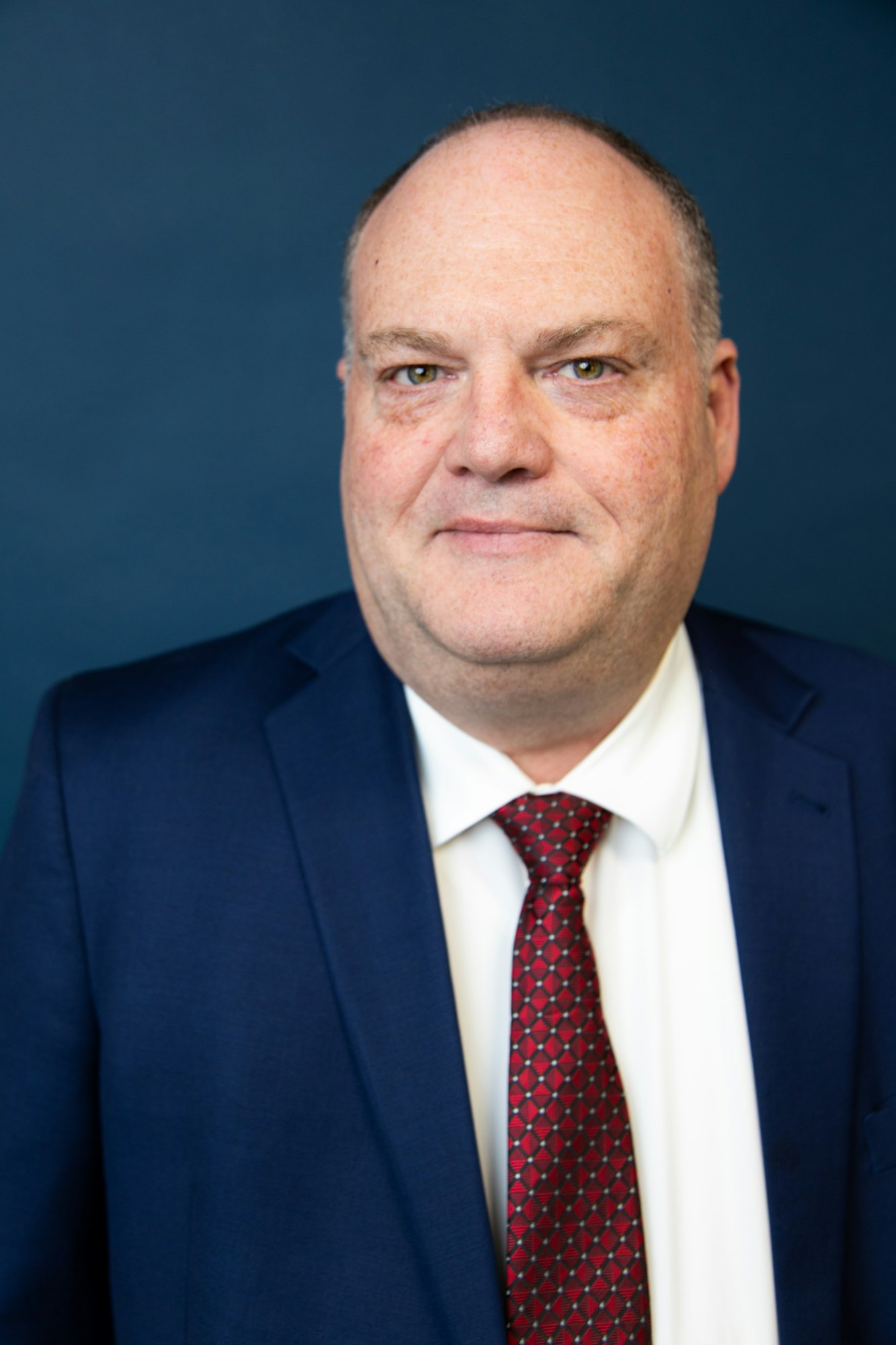 A man in a suit and tie with a white shirt, looking at the camera.