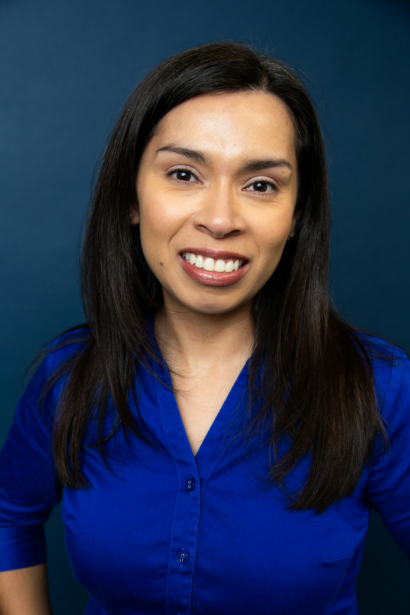 A smiling woman in a blue blouse against a blue background.