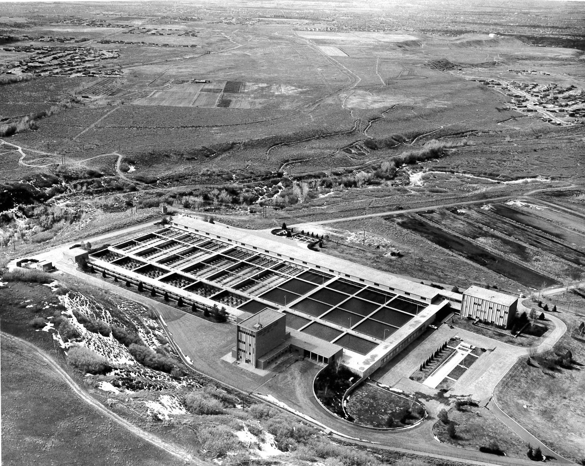 An aerial view of a large facility, likely a water treatment plant, surrounded by fields and distant structures.