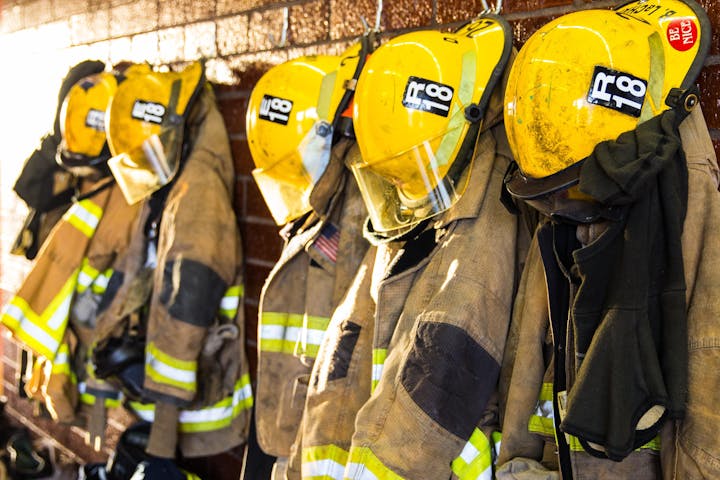 Five firefighter helmets and jackets hang on hooks in a fire station, showcasing equipment ready for service.