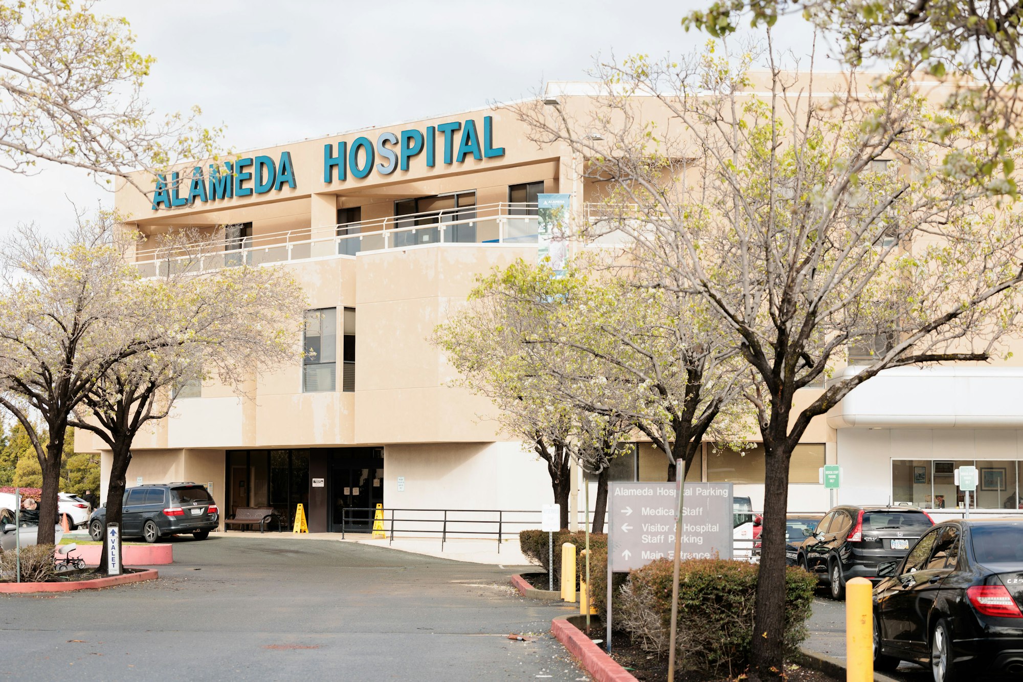 Exterior of Alameda Hospital with sign, trees, and parked cars.