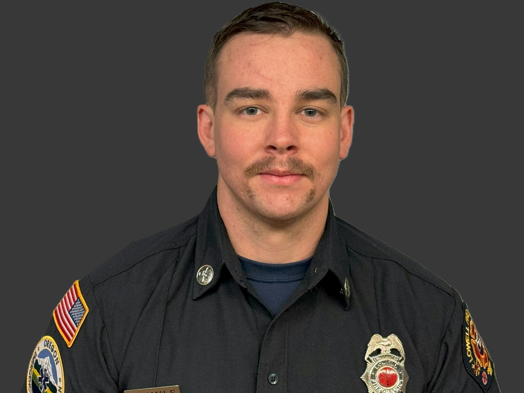 A man in a uniform with badges and patches on a dark background.