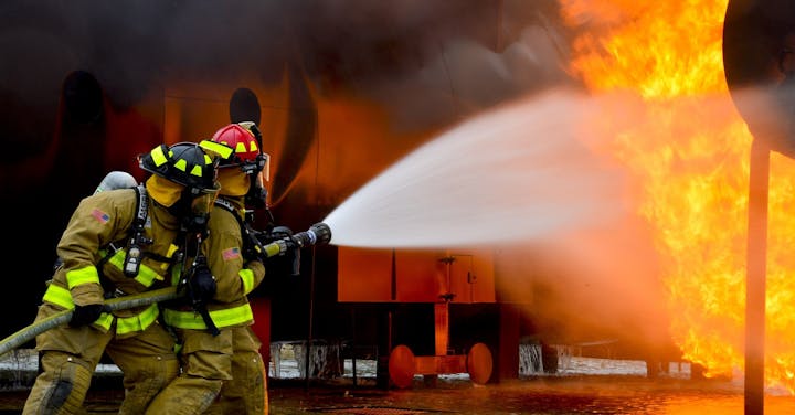 Two firefighters spray water on a large fire, showcasing their teamwork and bravery in a challenging situation.