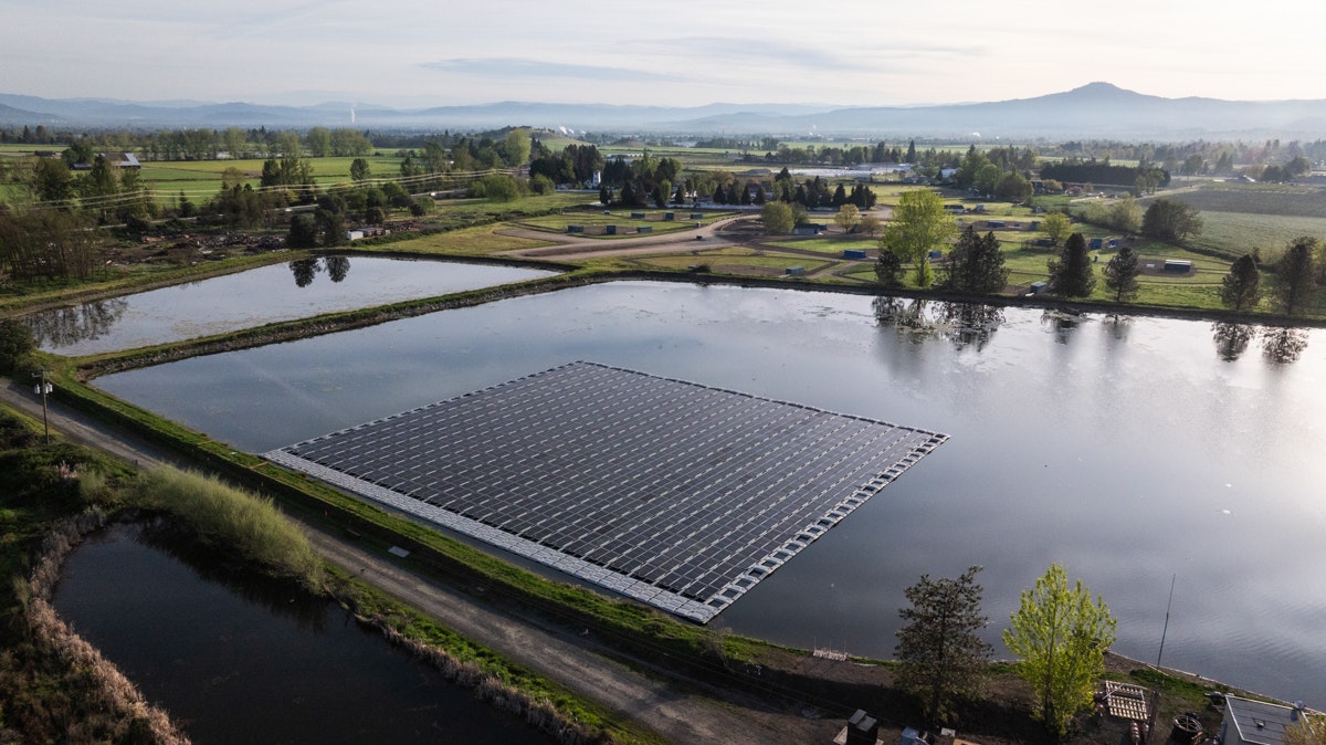 A floating solar panel installation on a pond, surrounded by green fields and trees, under a clear sky.
