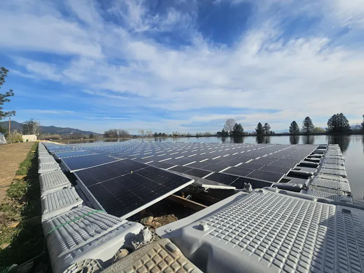 A floating solar panel installation on a body of water, surrounded by trees and a clear sky.