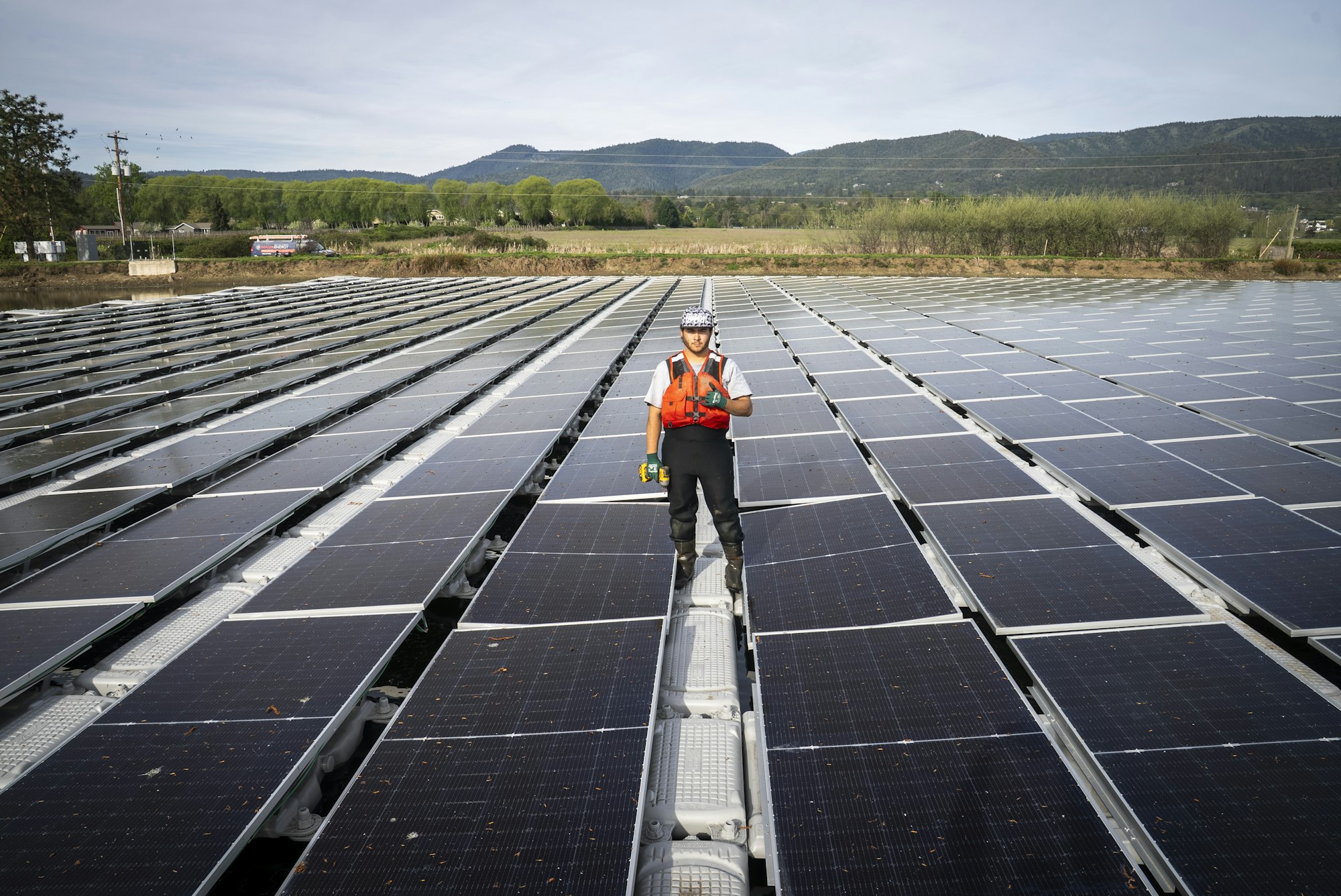 A worker stands on a floating solar panel installation, surrounded by rows of solar panels against a scenic backdrop.