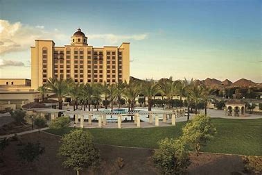 A large hotel with a dome, surrounded by palm trees, a pool, and a manicured lawn.