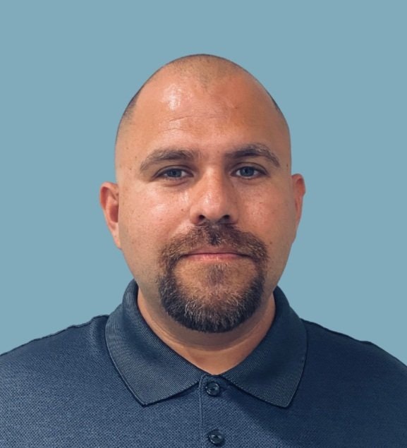 A man with a goatee, wearing a collared shirt, against a plain background.